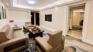 Habitación de hotel con sofá, una mesa de centro, un televisor de pantalla plana y piso alfombrado.