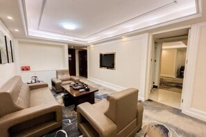 Ein Hotelzimmer mit einer Sofagruppe, einem Couchtisch, einem Flachbildfernseher und einem Teppichboden.