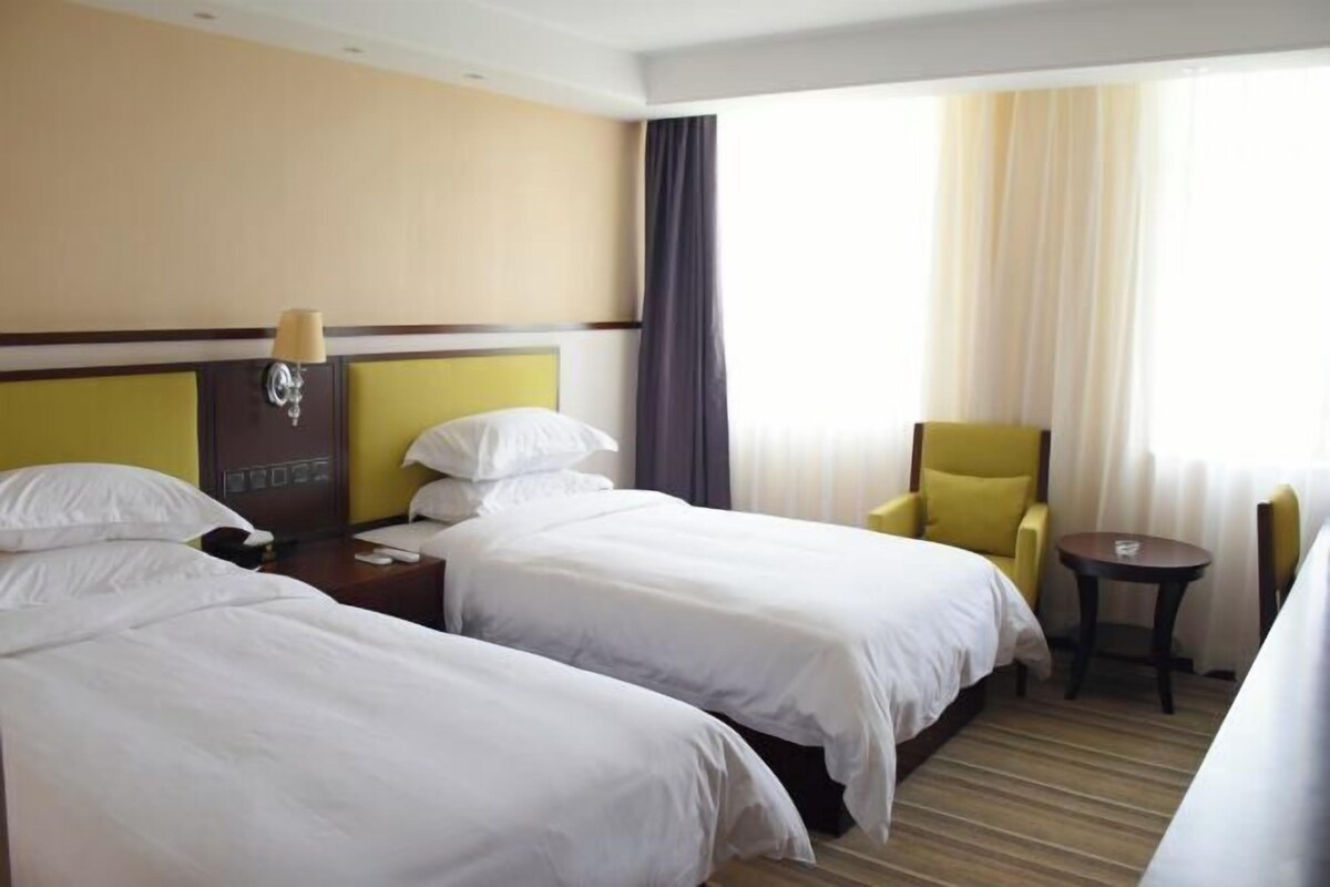 A hotel room with two beds, a small table, a chair, and a lamp.