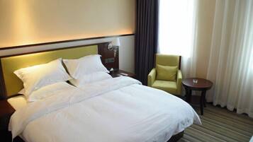A hotel room with a large bed, a nightstand, a lamp, a chair, and a small table.