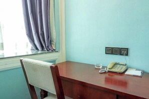 A wooden desk with a telephone and a glass of water, a chair, and a window with curtains.