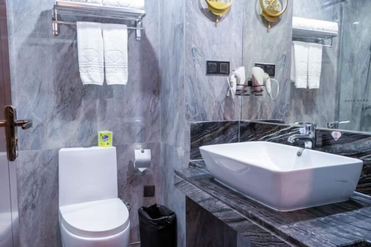 Un baño moderno con pared de mármol, inodoro blanco, un lavamanos grande y rectangular, y un espejo.