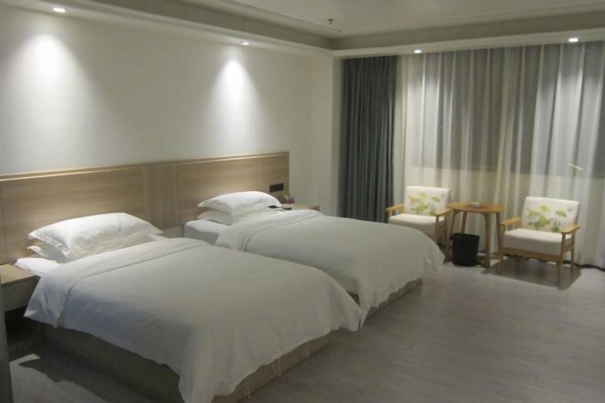 Habitación de hotel con dos camas, cabecero de madera, un ventanal con cortinas y dos sillas.