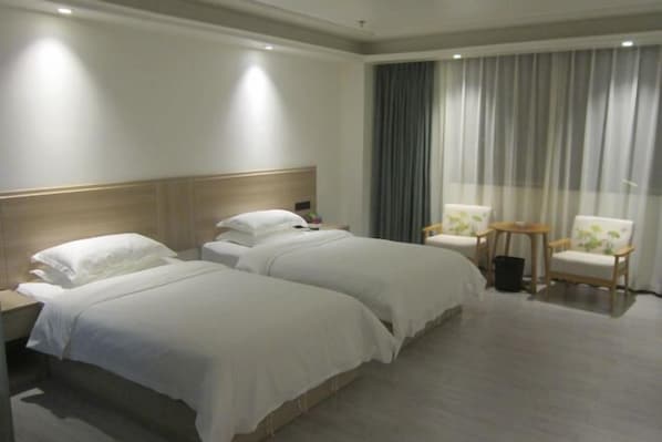 A hotel room with two beds, a wooden headboard, a large window with curtains, and two chairs.