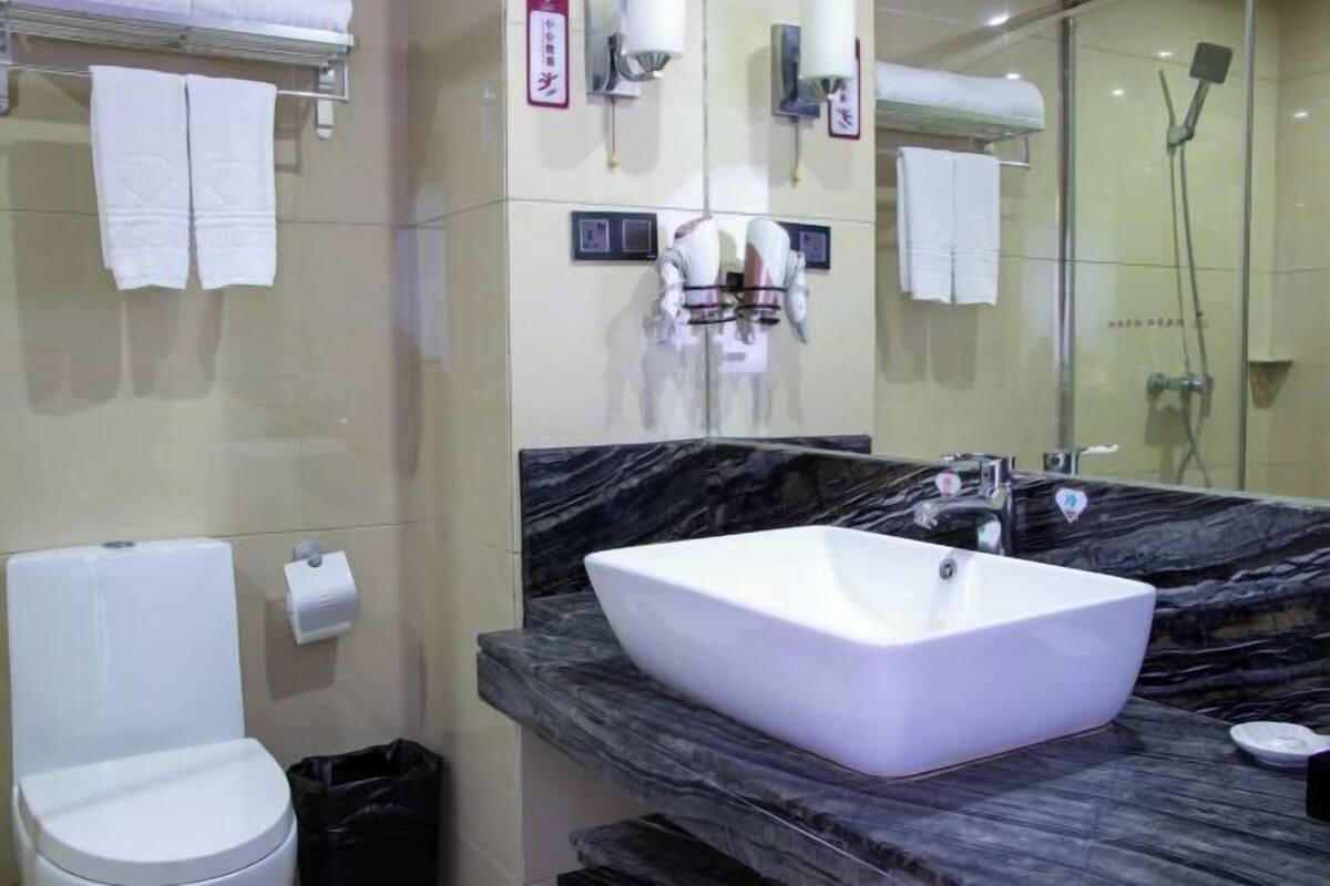 Un baño moderno con inodoro blanco, un lavamanos grande de color blanco sobre encimera de mármol y un box de ducha de vidrio.