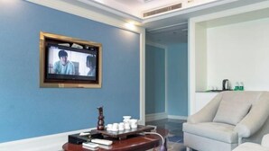 Habitación de hotel con una televisión en la pared, una pequeña mesa de madera con tazas y una bandeja, y un sillón beige.