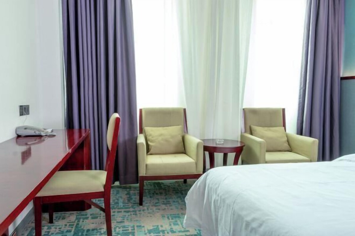 A hotel room with a bed, two armchairs, a small table, and a desk with a telephone.