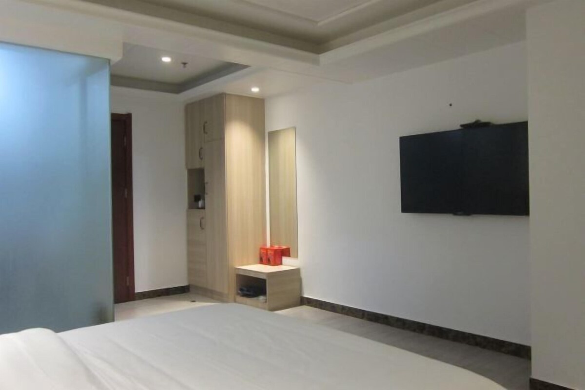 A hotel room with a bed, a TV mounted on the wall, a wardrobe, and a small table with a mirror.