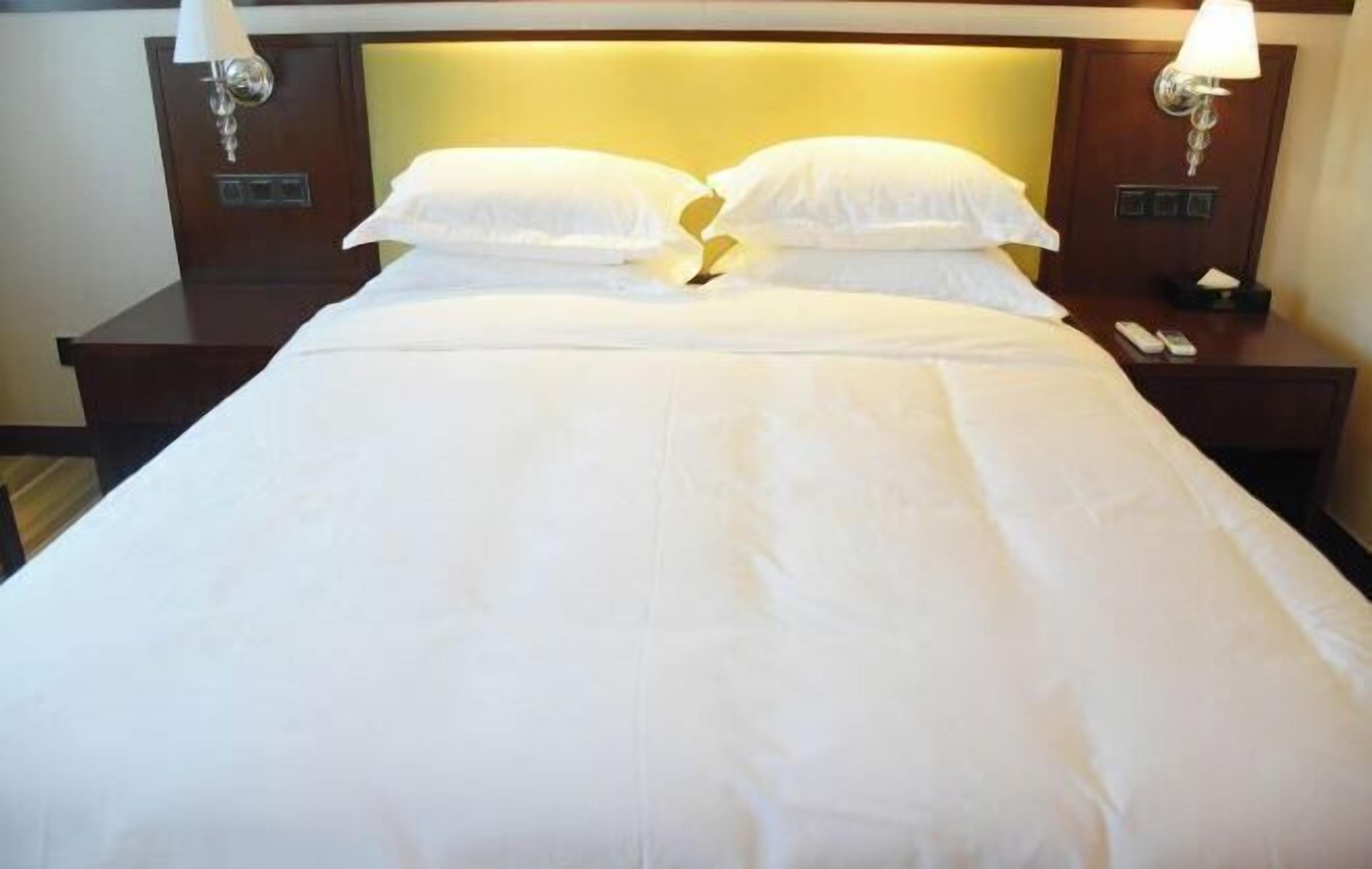 Una cama bien hecha con sábanas y almohadas blancas, dos mesitas de noche con lámparas y un cabecero con panel de luz.