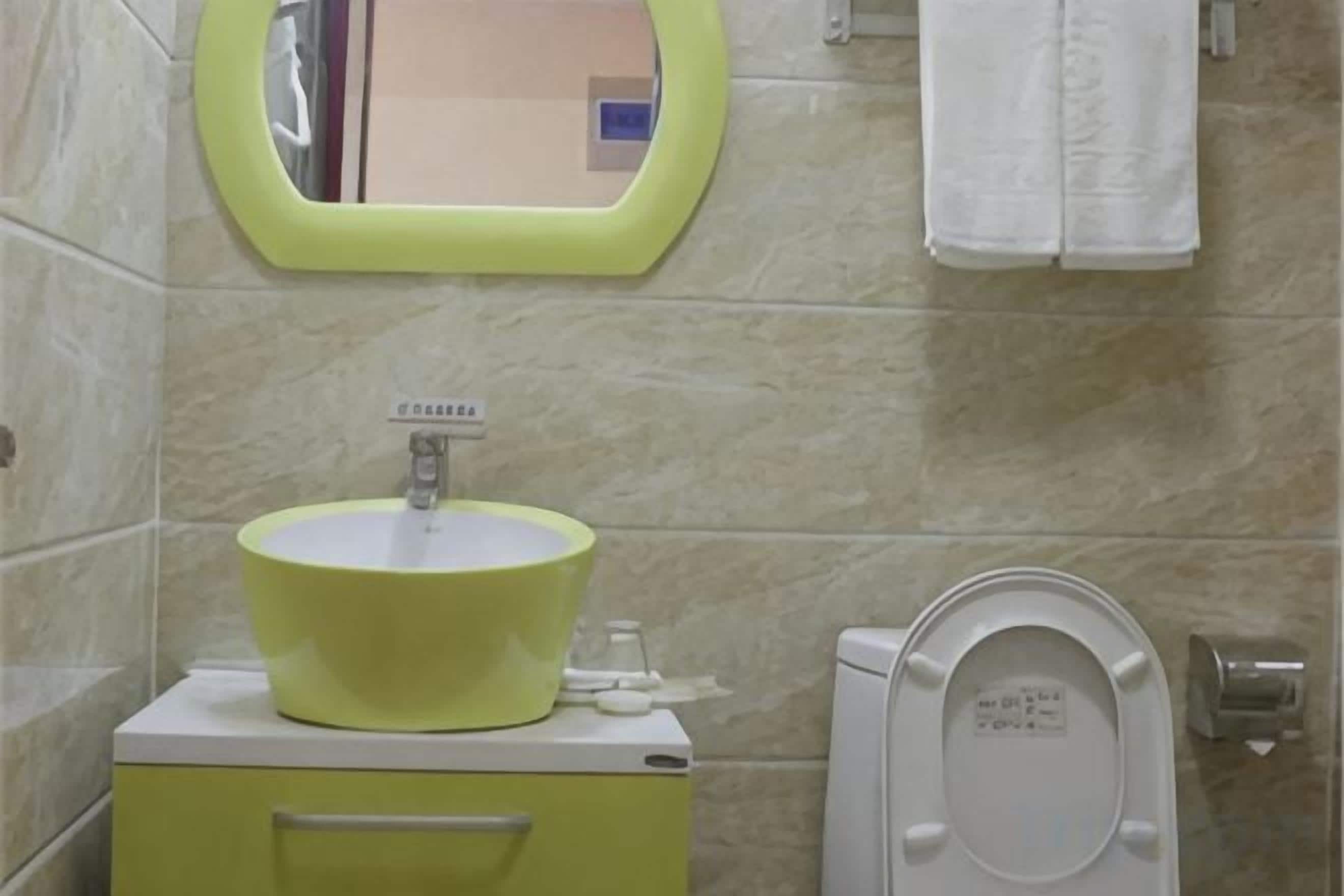 A bathroom with a yellow sink, a mirror, a toilet, and a towel hanging on the wall.