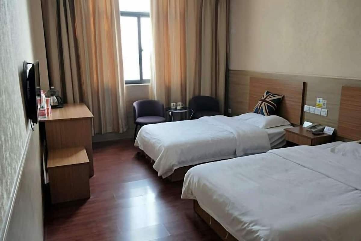 A hotel room with two beds, a desk, a chair, a TV, and a window with curtains.