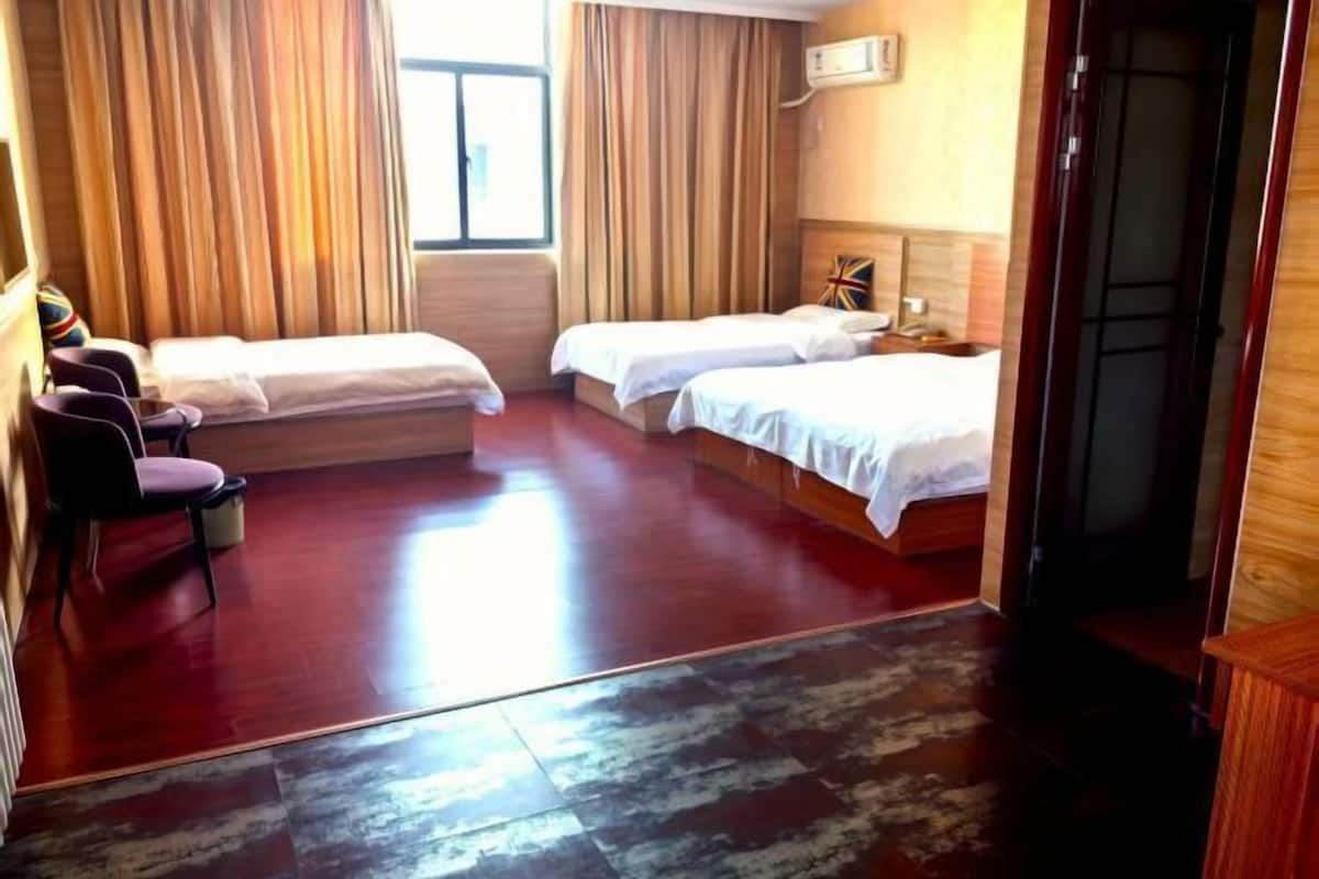 A hotel room with two beds, a seating area with chairs, a window with curtains, and a wooden floor.