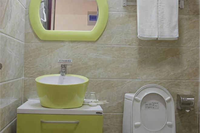 Un baño con un lavabo amarillo, un espejo, un inodoro y un perchero para toallas.