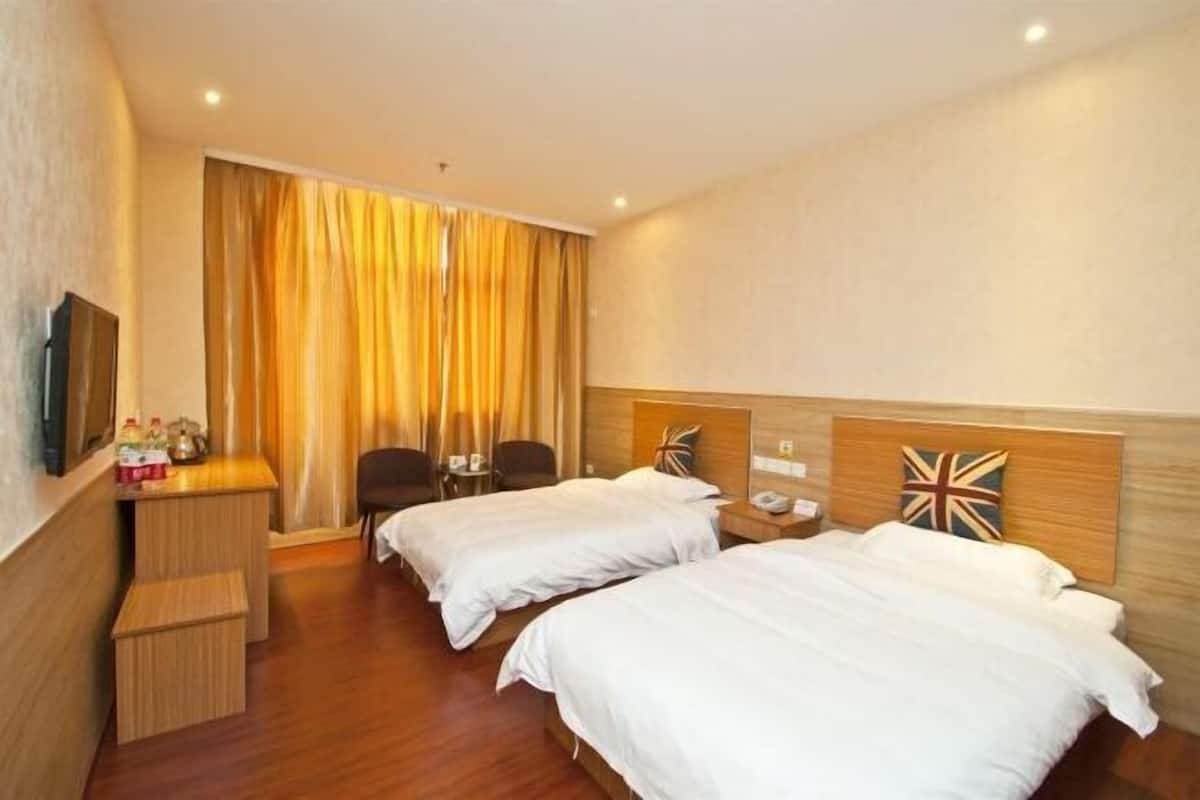 A hotel room with two beds, a desk, a chair, and a television.