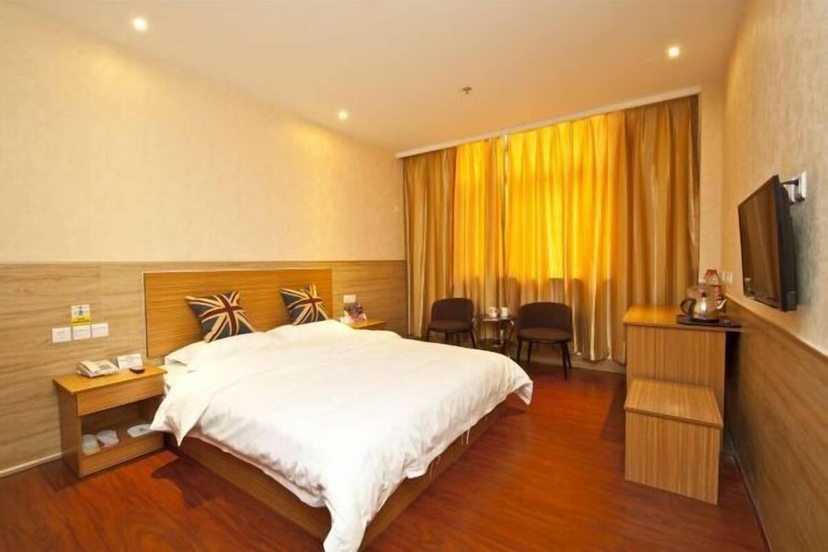 A hotel room with a large bed, a desk, two chairs, a television, and a window with curtains.