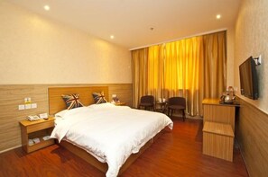 Una habitación de hotel con una cama grande, un escritorio, dos sillas, un televisor y una ventana con cortinas.