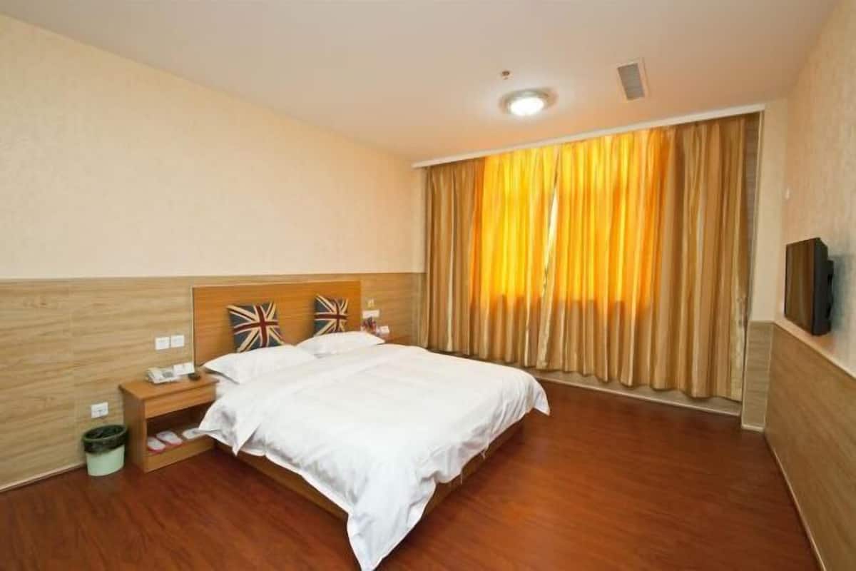 A hotel room with a bed, bedside table, nightstand, and a large window with curtains.