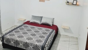 A bedroom with a bed, two pillows, a chandelier, an air conditioner, a wall-mounted shelf with decorative items, and a marble-tiled floor. - Appartement de 150m2 Proche Dune Belle Plage (Marsa Ben M'Hidi)