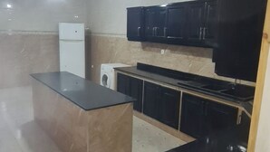 A kitchen with a central island, black cabinets, a refrigerator, and a washing machine. - Appartement de 150m2 Proche Dune Belle Plage (Marsa Ben M'Hidi)