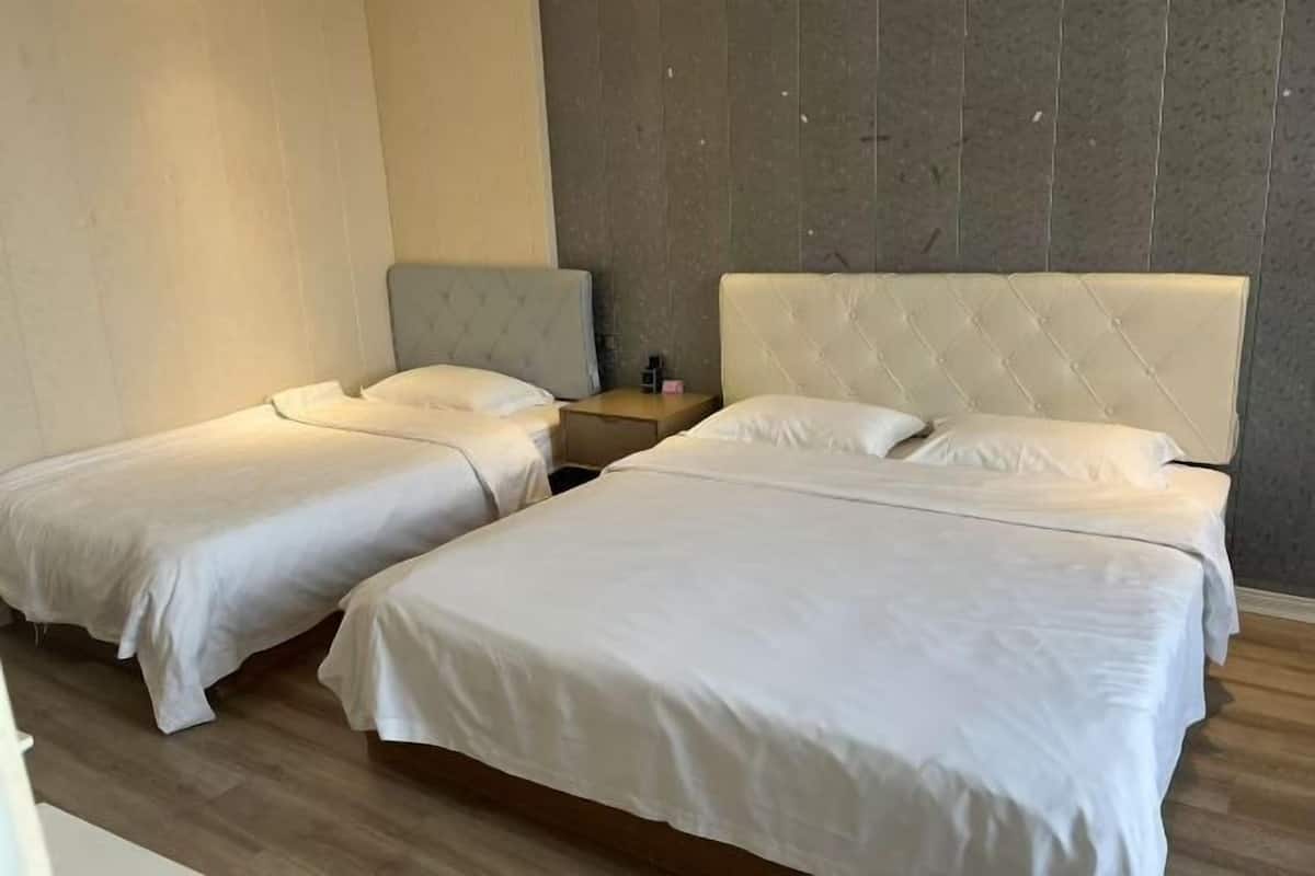 Une chambre d’hôtel avec deux lits simples, un plancher en bois et un mur gris à la texture particulière.