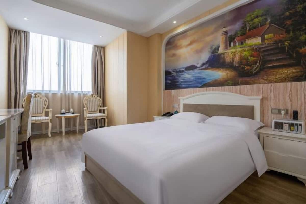 Une chambre d’hôtel avec un grand lit, deux tables de chevet, un bureau et deux chaises.