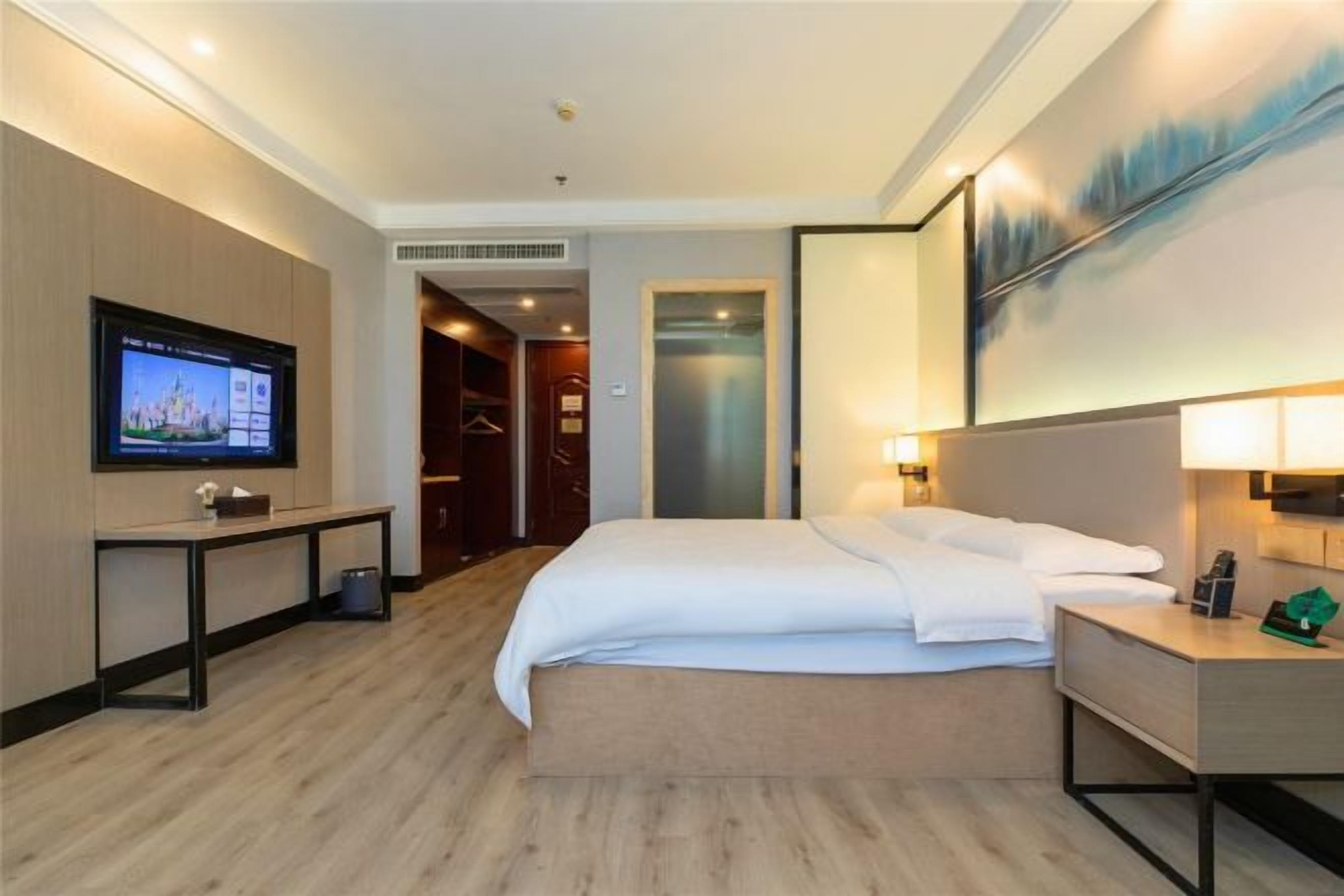 A hotel room with a bed, bedside table, TV, and a painting on the wall.