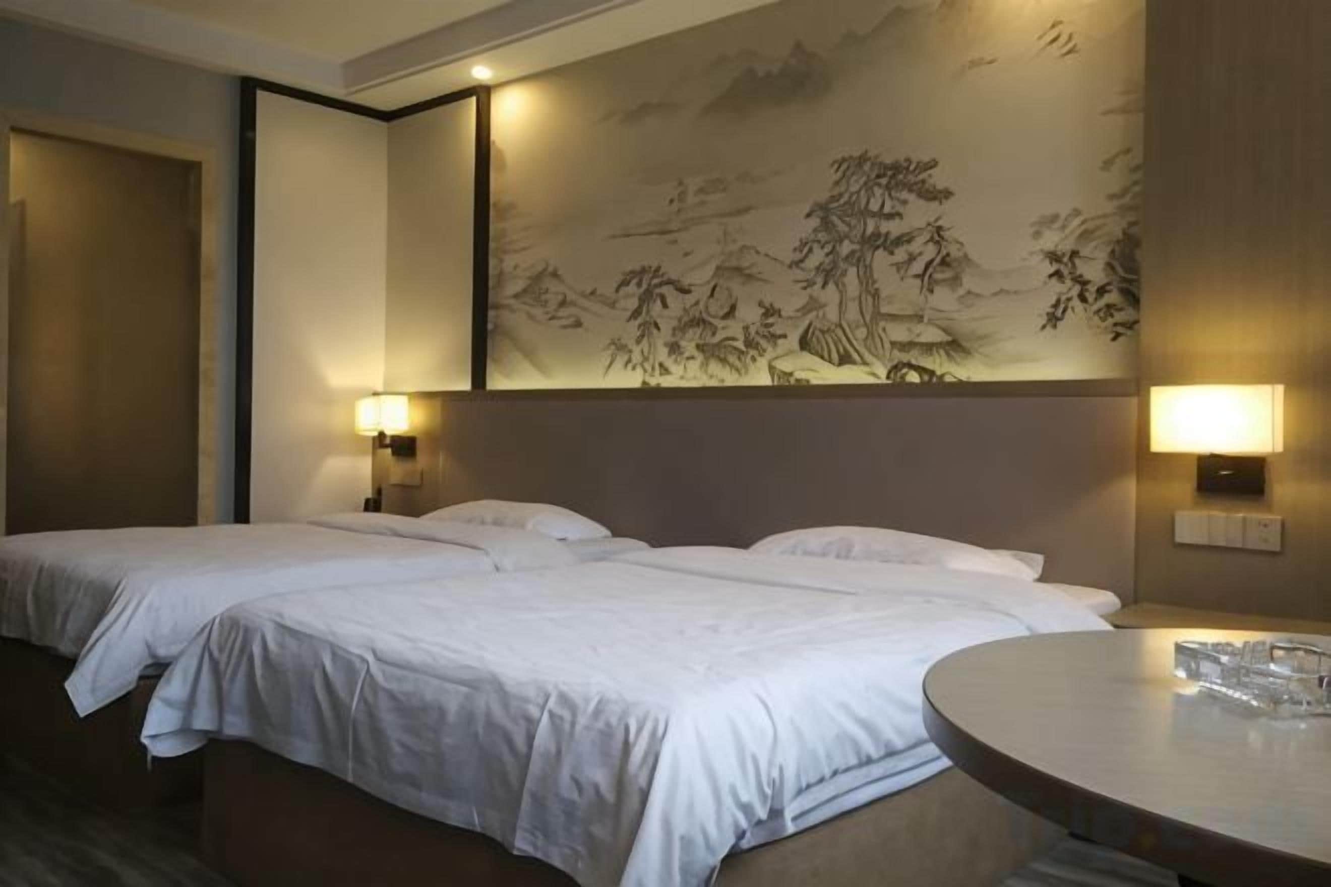 Habitación de hotel con dos camas, una mesa redonda y una obra de arte en la pared.