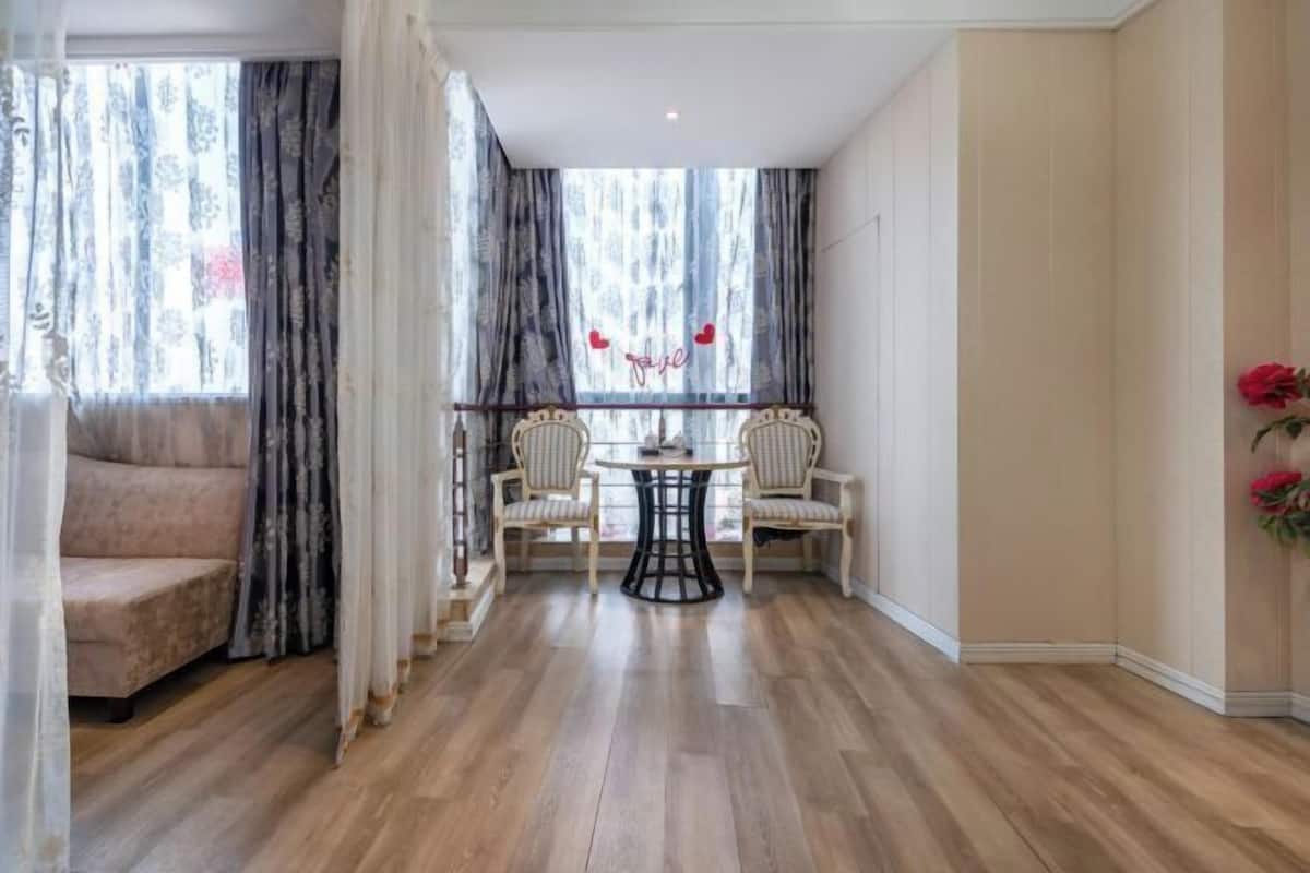 Une pièce avec un plancher en bois, un canapé, une table à manger avec des chaises et une fenêtre avec des rideaux.