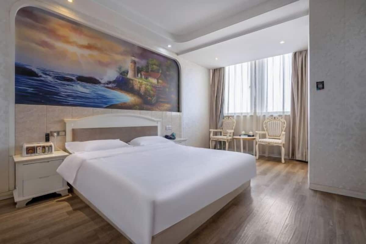 Une chambre d’hôtel avec un grand lit, une table de chevet, une chaise et un tableau au mur.