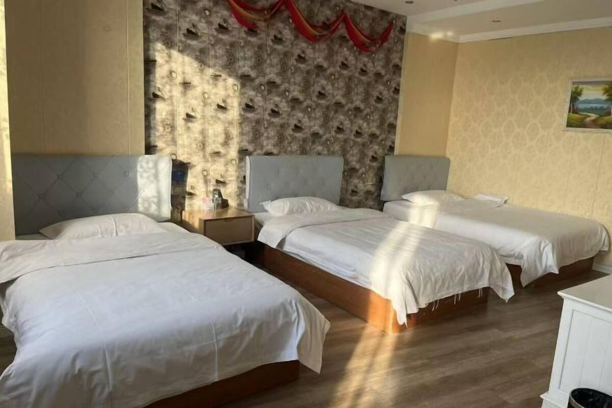 Une chambre d’hôtel avec trois lits simples, un mur orné d’un motif et un tableau accroché au mur.