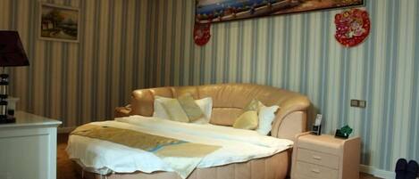 A bedroom with a large round bed, a bedside table, a nightstand, and a wall-mounted painting.