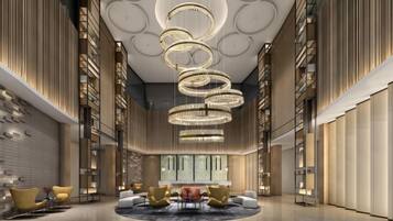 A spacious lobby with a circular seating area, a large chandelier, and bookshelves along the walls.