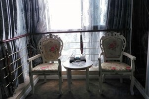 Dos sillas con tapicería floral, una mesita redonda con tetera y taza, y una ventana con cortinas.