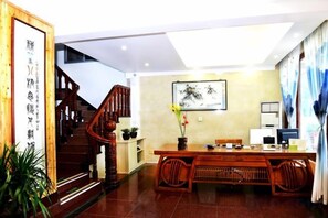Une pièce de style chinois traditionnel, avec un escalier en bois, une table à manger entourée de chaises et une œuvre calligraphique encadrée accrochée au mur.