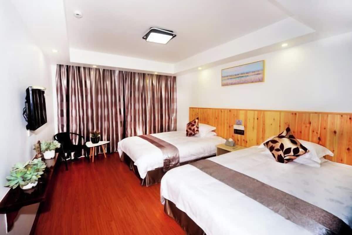 A hotel room with two beds, a wooden headboard, a flat-screen TV mounted on the wall, a small table, and a chair.
