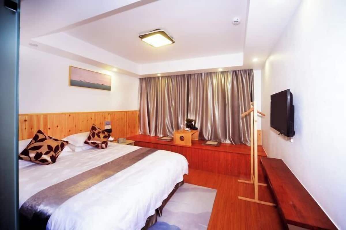 A hotel room with a wooden headboard, a bed with patterned pillows, a flat-screen TV, and a bench.