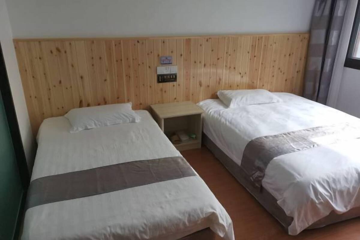 A room with two beds, wooden headboard, a nightstand, and a window.