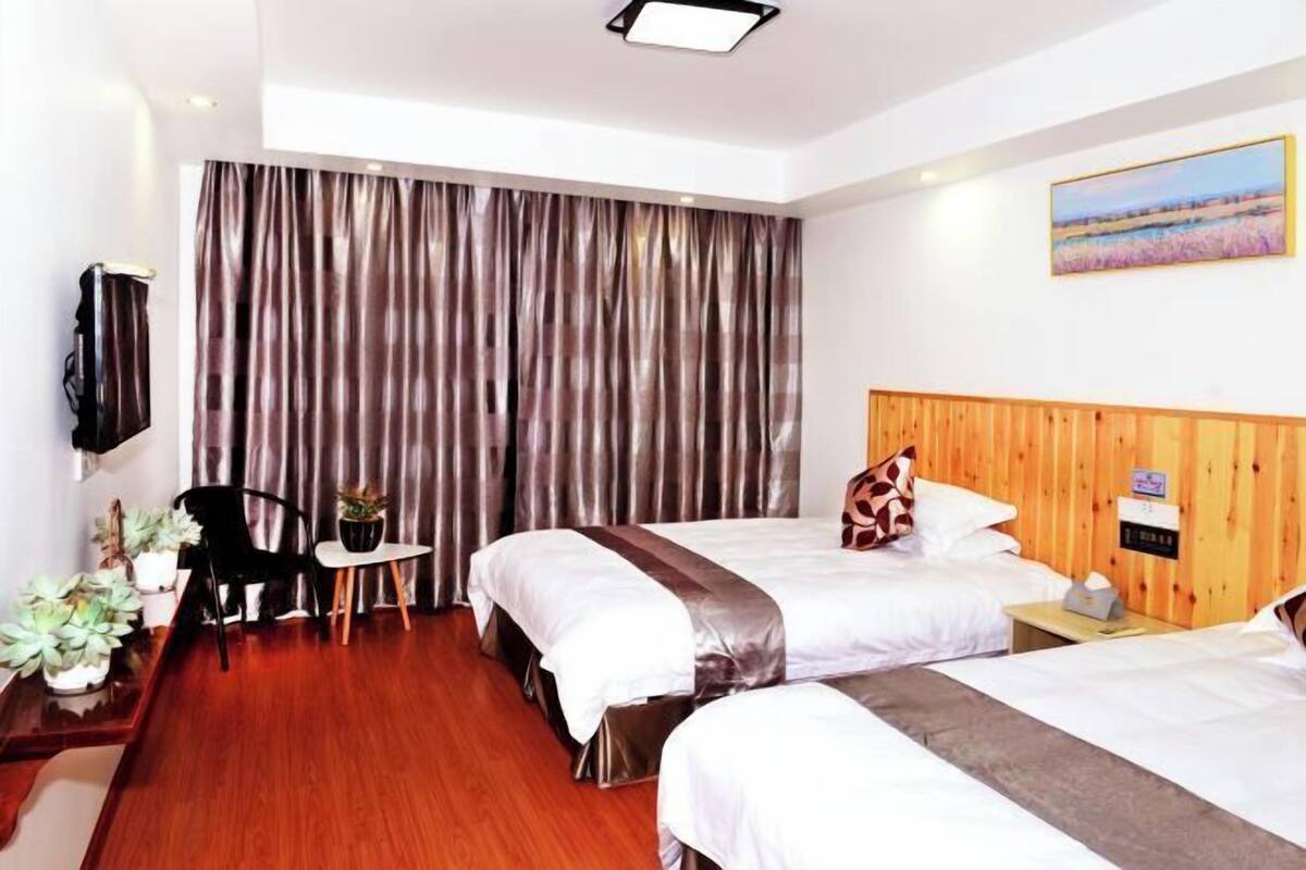 A hotel room with two beds, a wooden headboard, a small table with a chair, and a TV mounted on the wall.