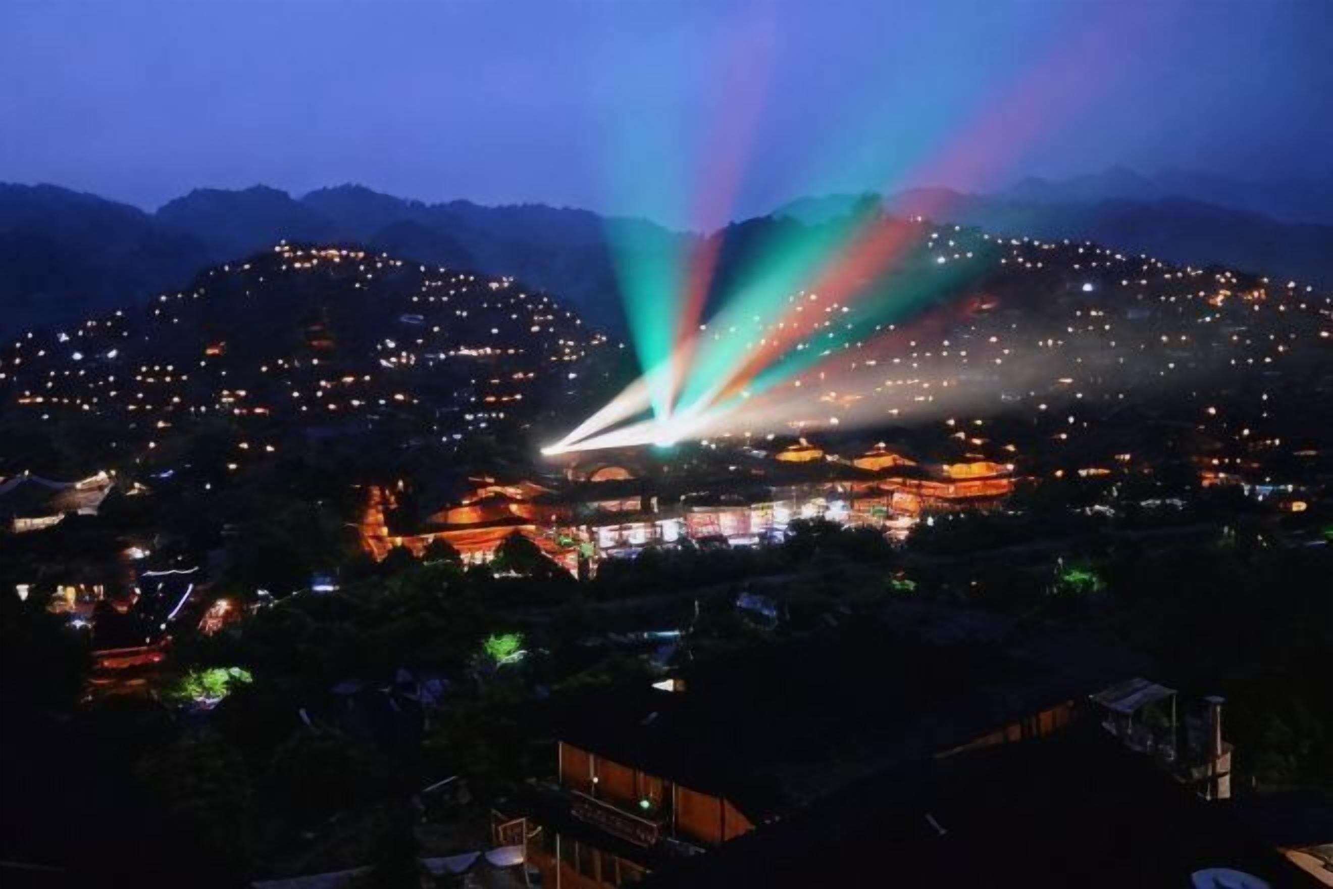 A nighttime view of a town with illuminated buildings and a prominent structure with a light beam.