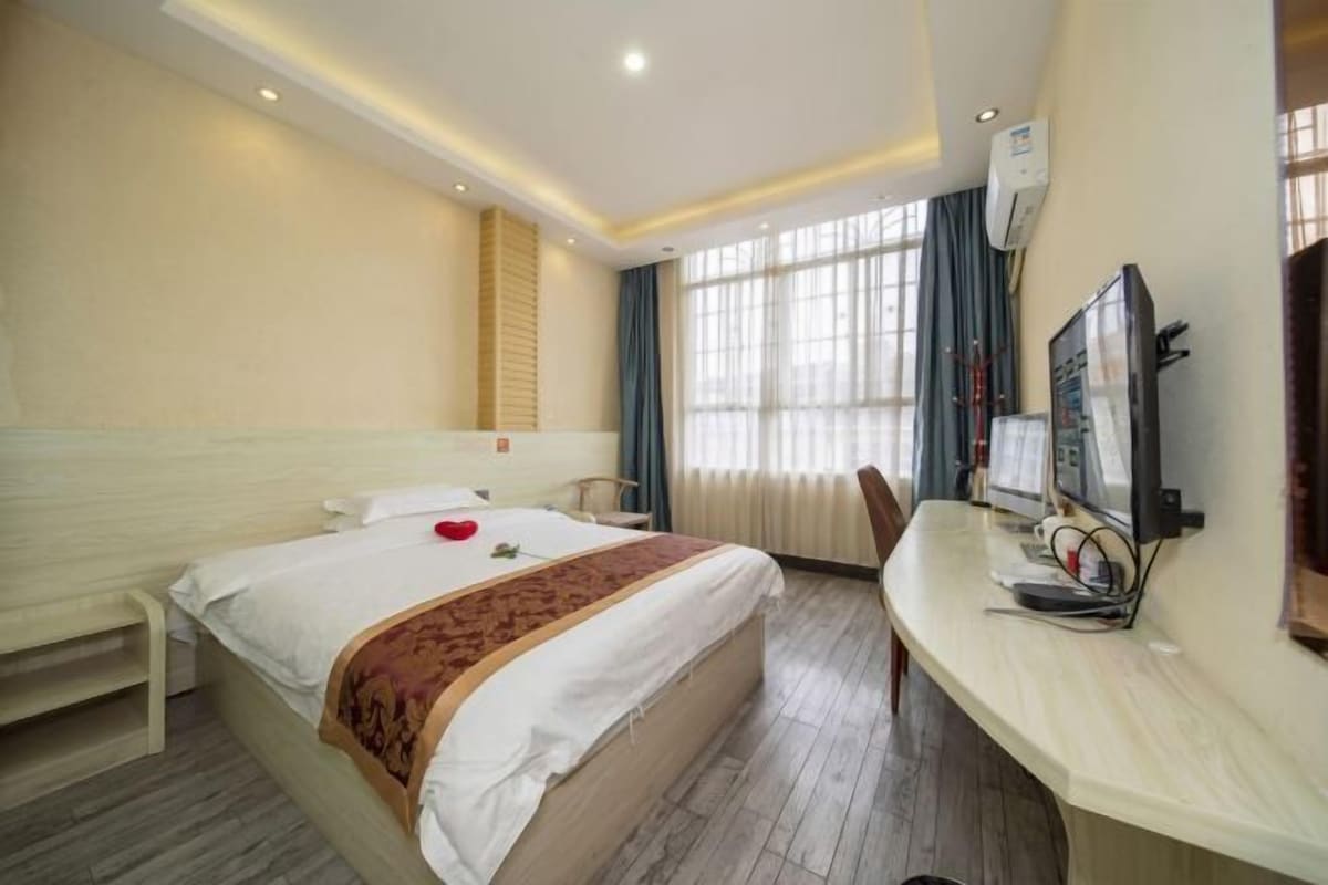 A hotel room with a large bed, a desk with a computer, and a window with curtains.
