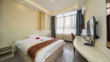 A hotel room with a large bed, a desk with a computer, and a window with curtains.