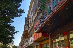 Un edificio de varios pisos con diversos comercios en la planta baja, incluyendo un escaparate con un letrero rojo.