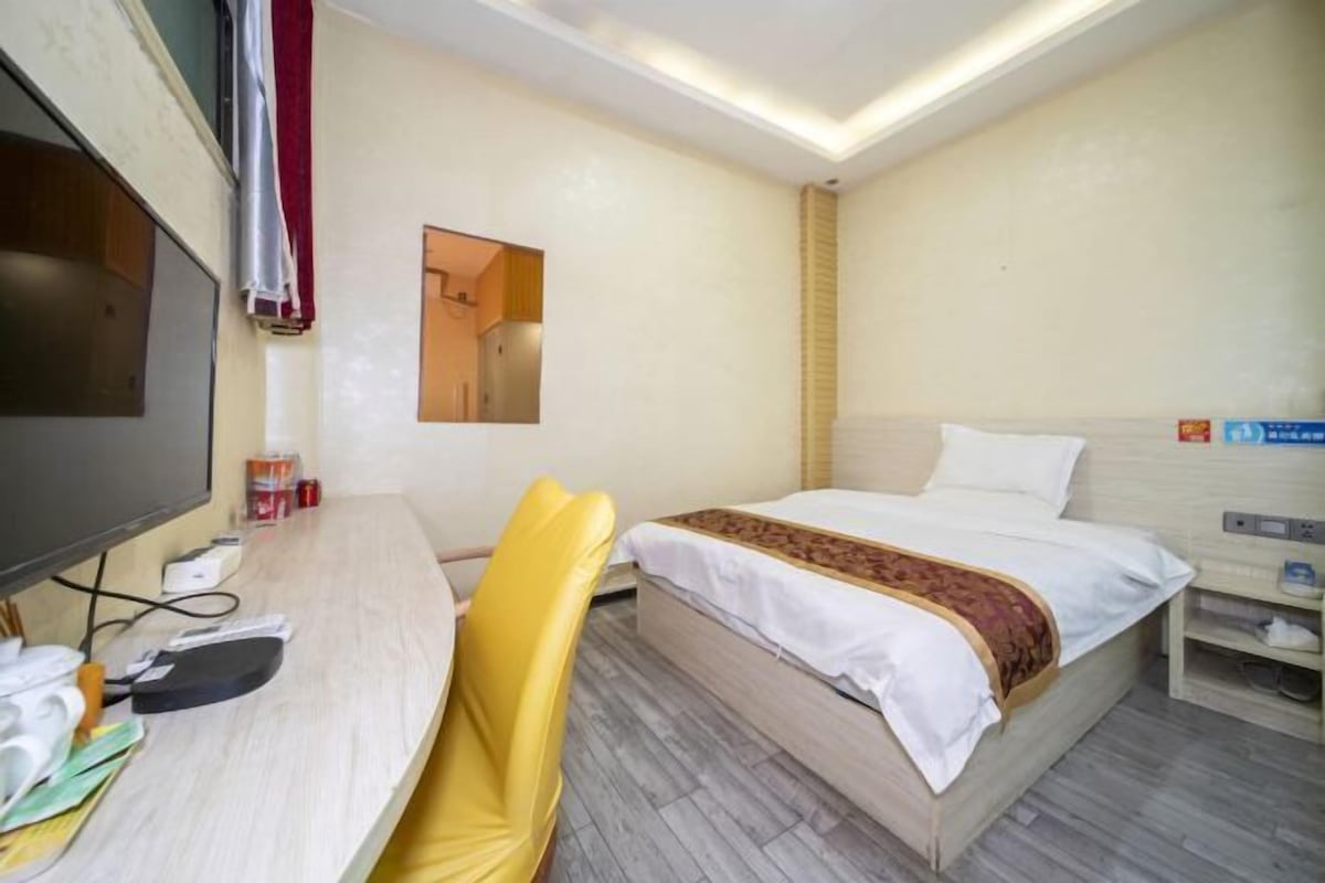 A hotel room with a bed, a desk with a chair, a TV, and a small table with a lamp.