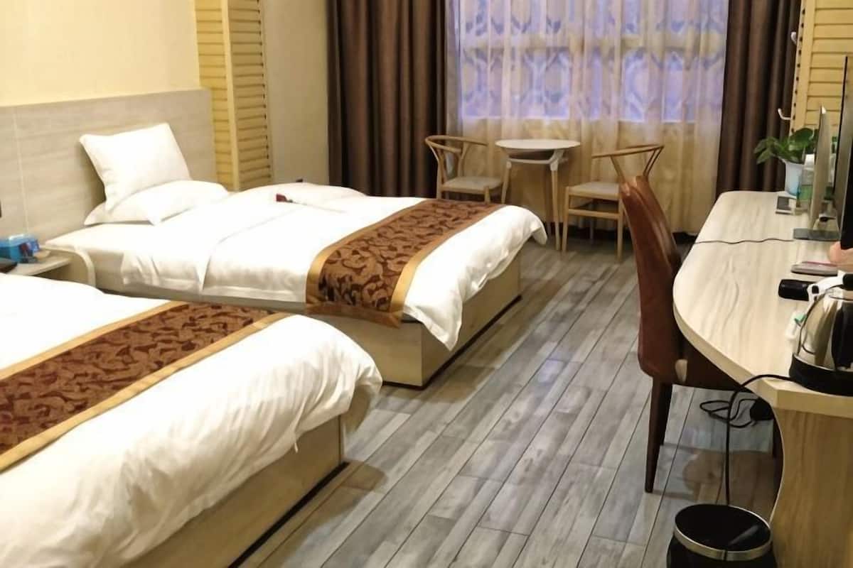 Quarto de hotel com duas camas, uma escrivaninha, uma cadeira e uma mesa pequena.