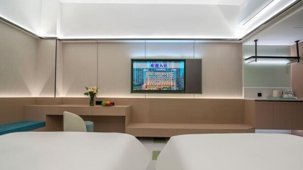 Moderni hotellihuone, jossa on seinälle asennettu taulutelevisio, pieni oleskelualue ja minikeittiö.