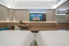 Ein modernes Hotelzimmer mit Flachbildfernseher an der Wand, einer kleinen Sitzecke und einer Küchenzeile.
