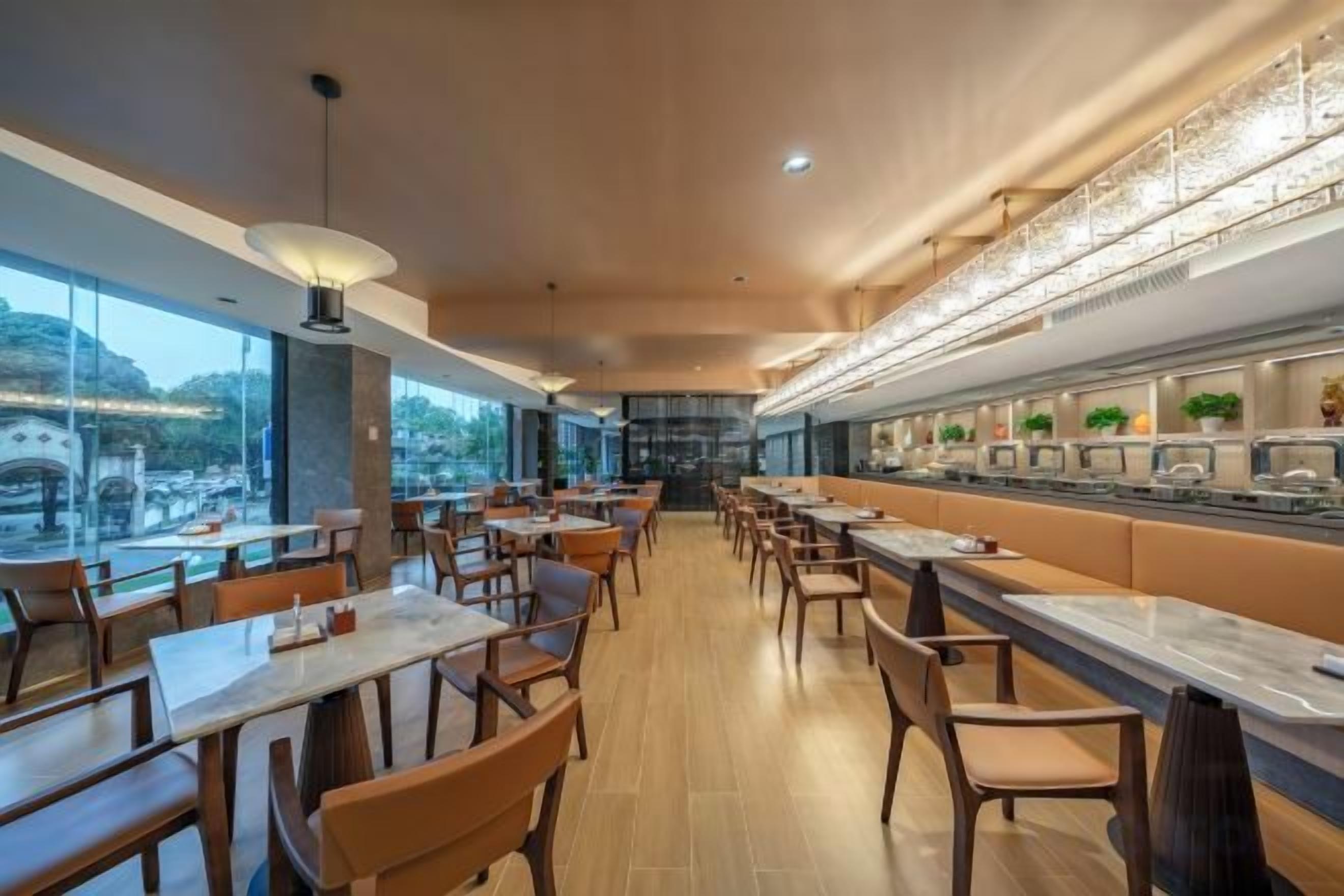 Un restaurant doté d’un long comptoir, de plusieurs tables et chaises, et offrant une vue sur le paysage urbain grâce à de grandes fenêtres.