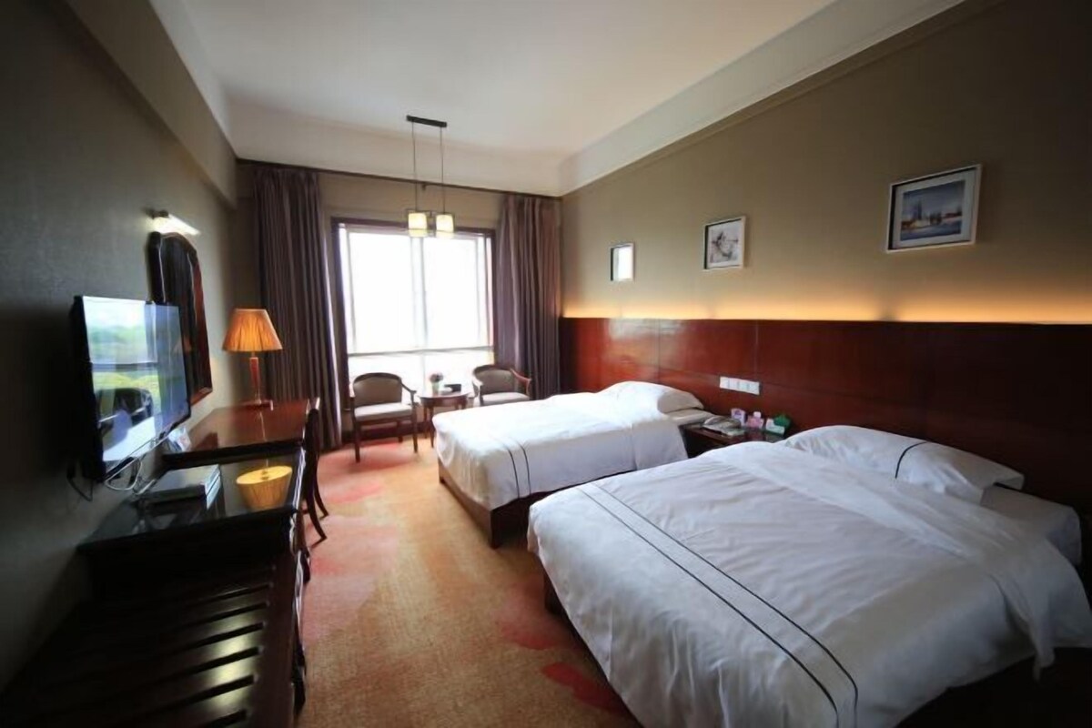 Habitació d'hotel amb dos llits, un escriptori amb un televisor, una làmpada i una finestra amb cortines.