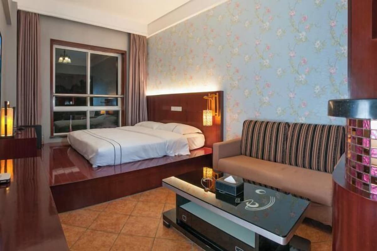 Habitació d'hotel amb llit, sofà, taula de cafè i una finestra gran.