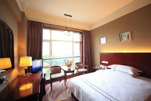 A hotel room with a bed, a desk with a lamp, a television, two chairs, a small table with a vase, and a window with curtains. - Century Holiday Hotel (Baise)